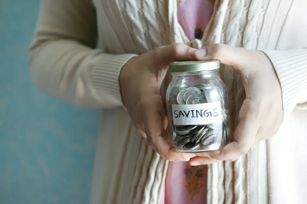 Woman Holding a Jar of Coins with Savings Written on It 