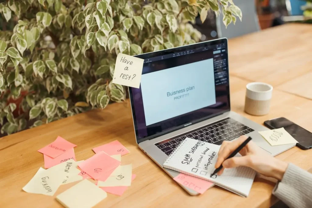 A Person Working on a Business Plan on a Laptop While Taking Notes